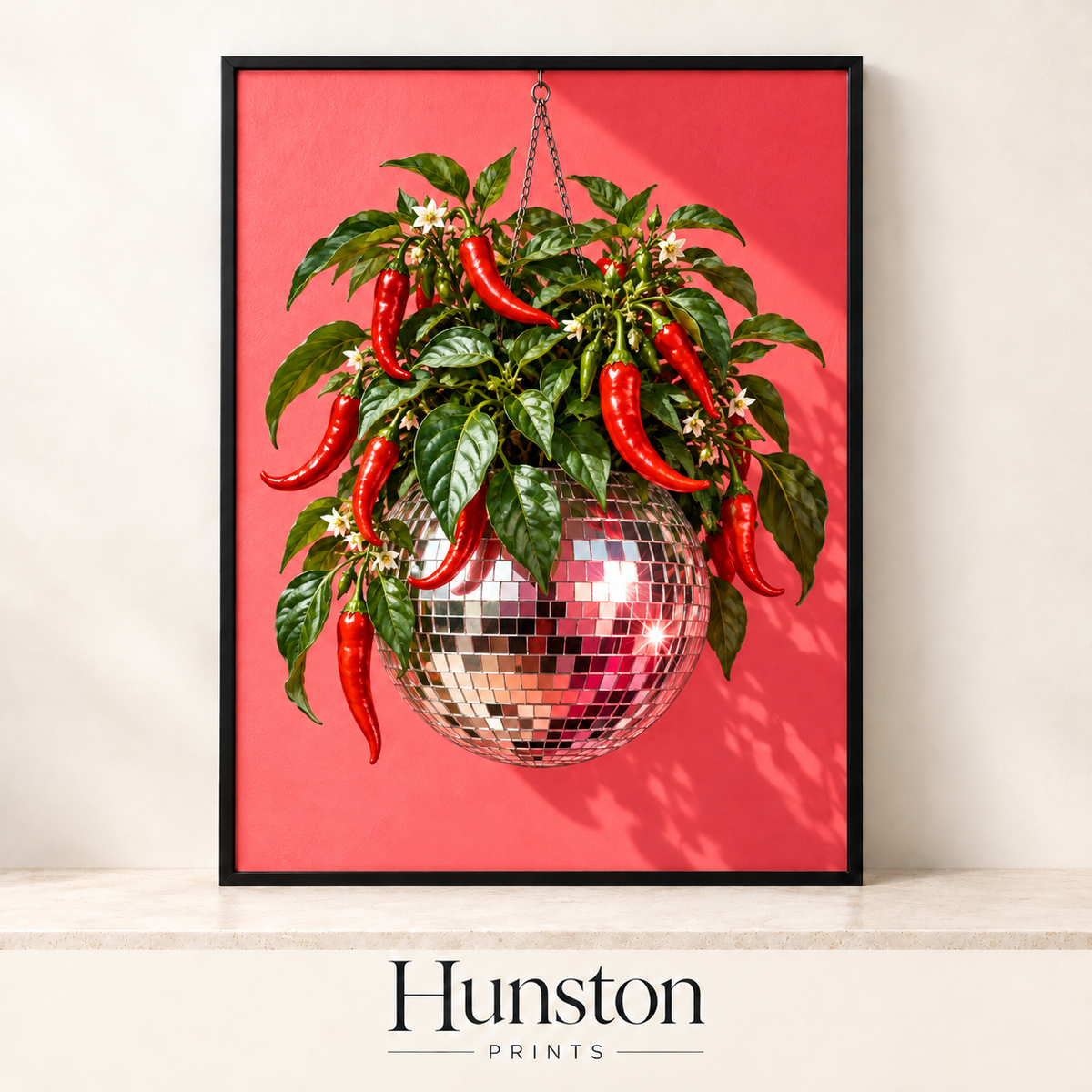 Red chilli plant growing out of a hanging disco ball on a coral background