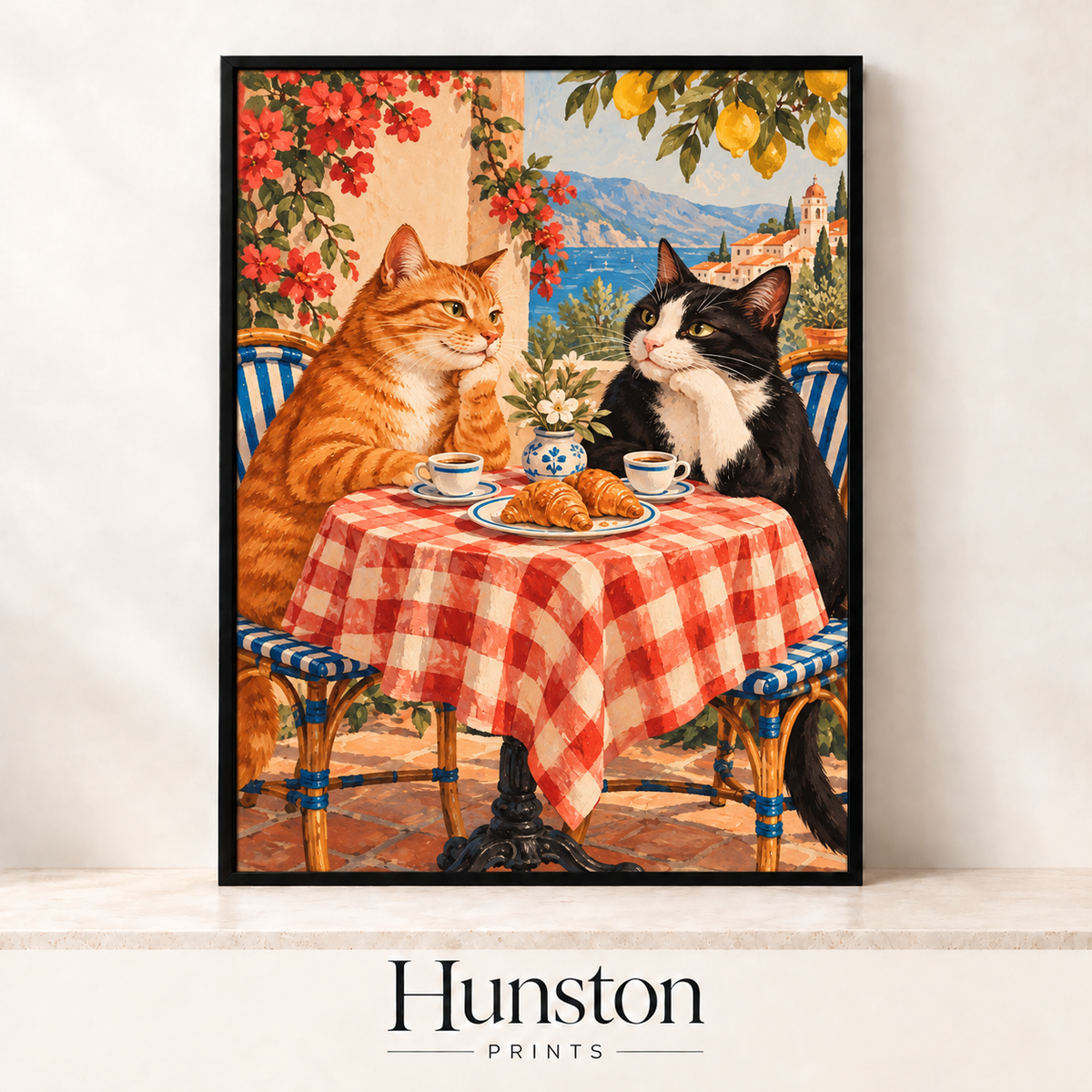 Ginger cat and black and white cat having coffee and croissants at a gingham table