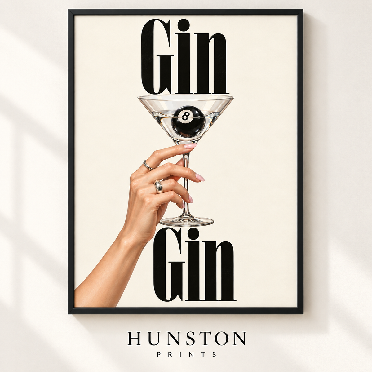 Hand holding a martini glass with a black 8 ball inside between the words Gin Gin