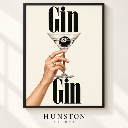 Hand holding a martini glass with a black 8 ball inside between the words Gin Gin
