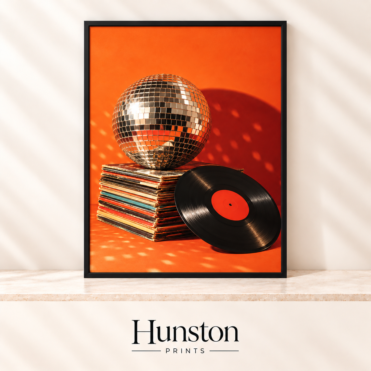 Mirror disco ball on a stack of record sleeves beside a vinyl LP on an orange background