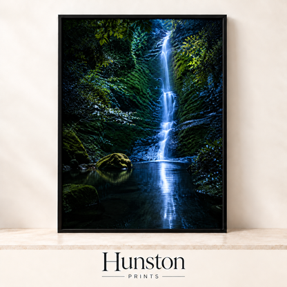 Slender waterfall falling into a dark pool in a mossy gorge