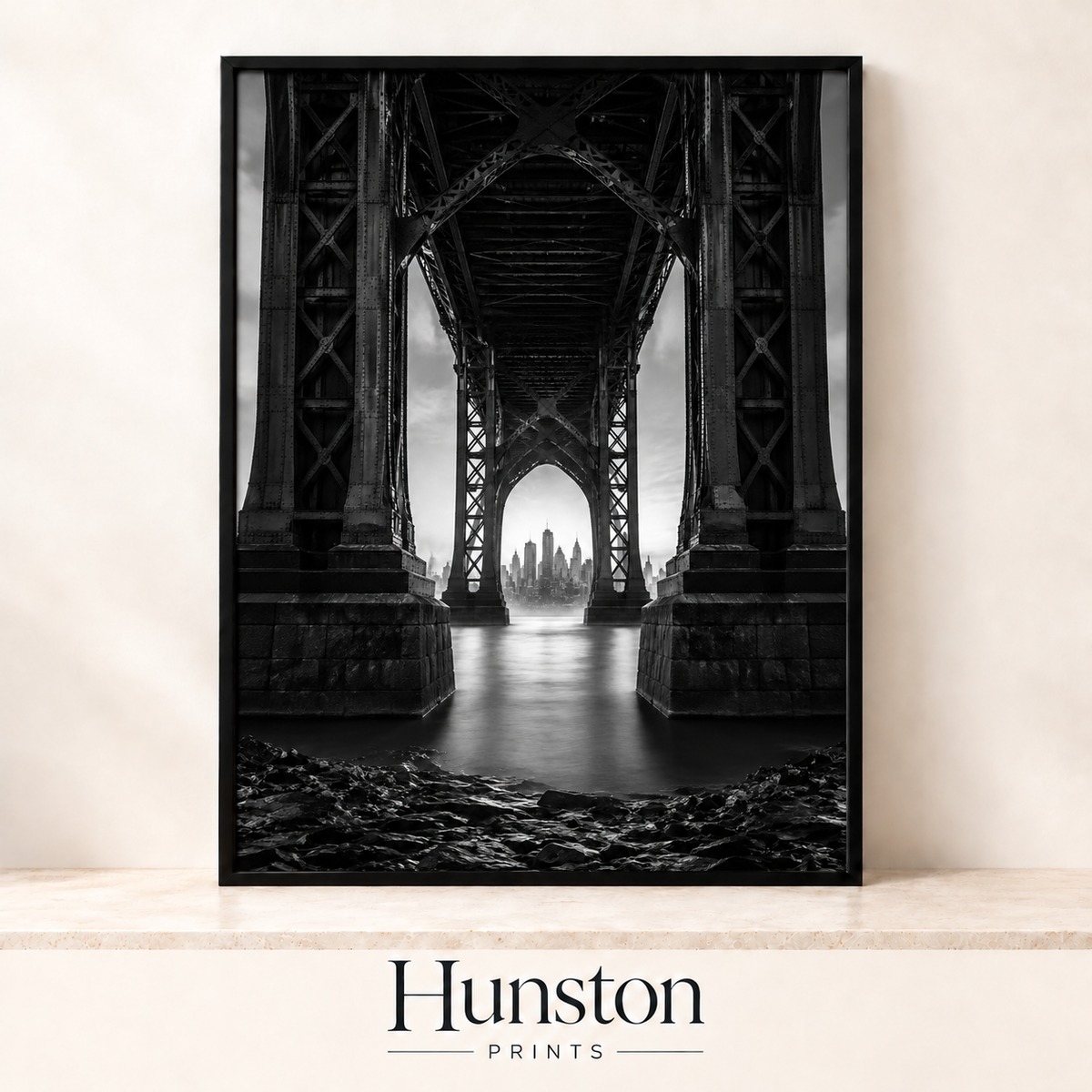 Black and white view of a city skyline framed beneath a steel bridge