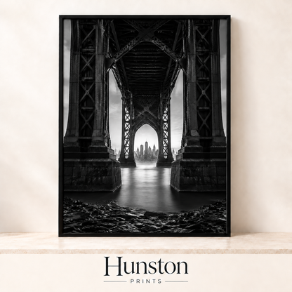 Black and white view of a city skyline framed beneath a steel bridge