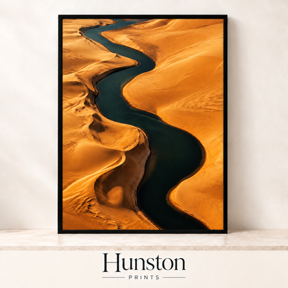 Aerial view of a dark river winding through golden sand dunes