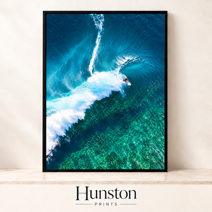Aerial view of a surfer riding a white wave over a turquoise reef